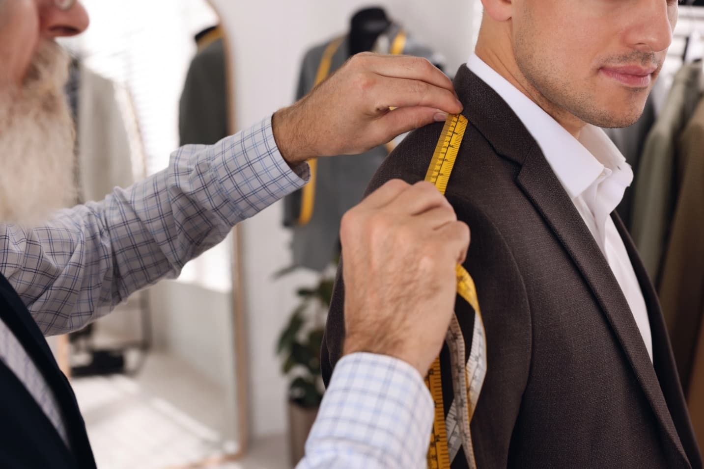 Professional tailor measuring shoulder seam length on client's jacket in atelier, close-up.