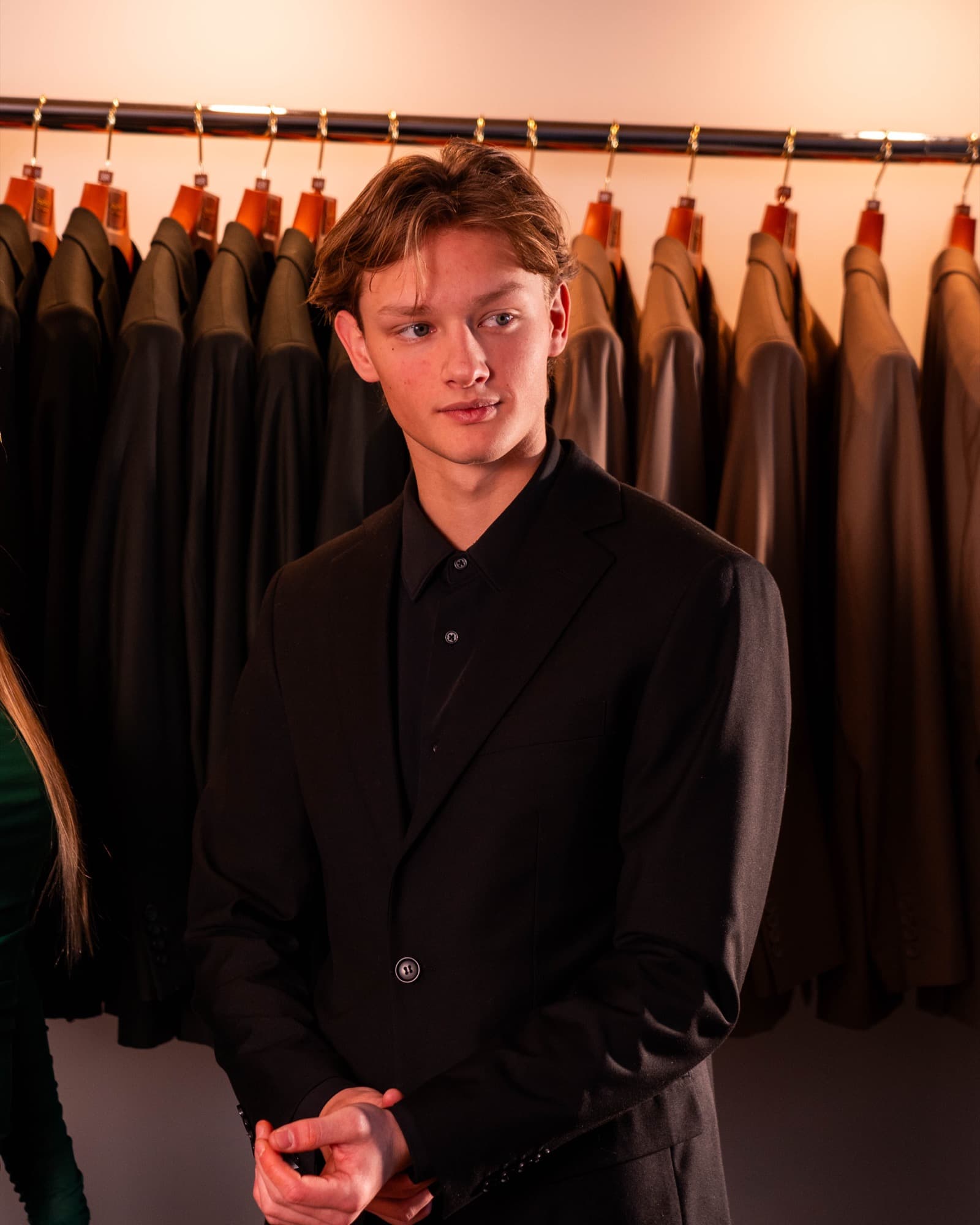 Model portrait in all-black suit with suits in background